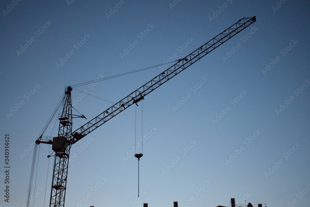 Industrial construction building crane against cloudy sunset sky in background Industrial construction building crane against cloudy sunset sky in background