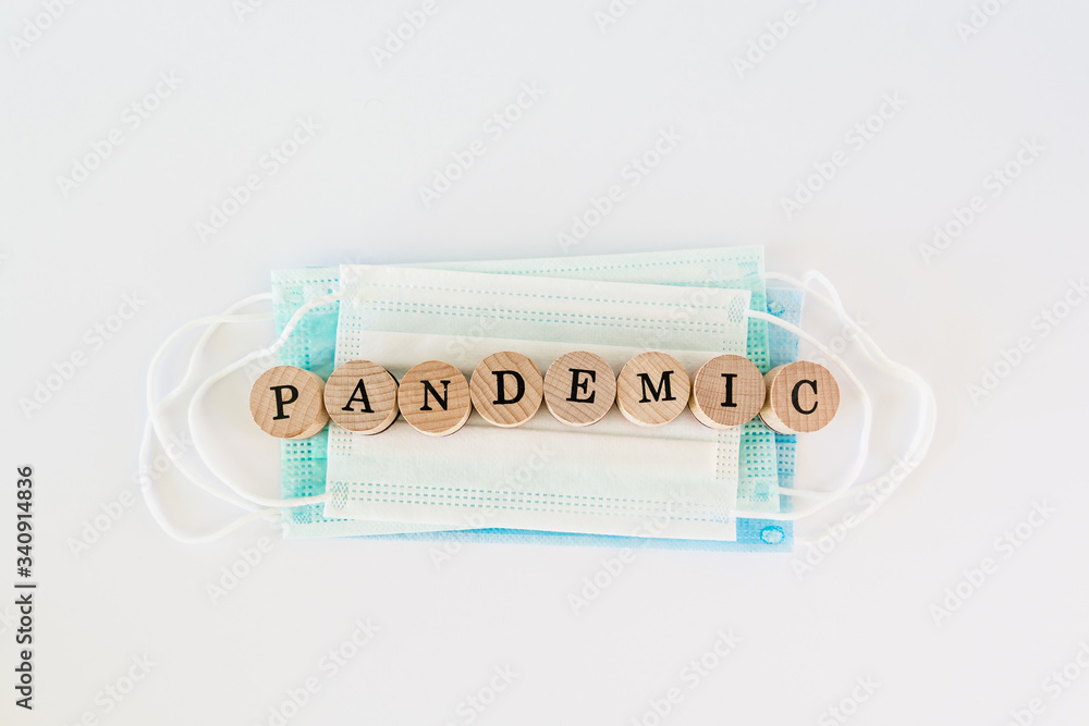 Word pandemic written with wooden blocks with black letters laying on protective disposable surgical masks Word pandemic written with wooden blocks with black letters laying on protective disposable surgical masks