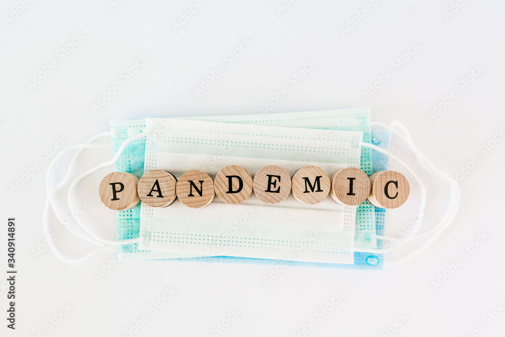 Word pandemic written with wooden blocks with black letters laying on protective disposable surgical masks Word pandemic written with wooden blocks with black letters laying on protective disposable surgical masks
