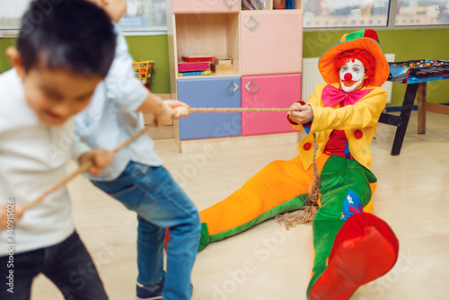 Tableau sur toile Clown and joyful little boys playing tug of war