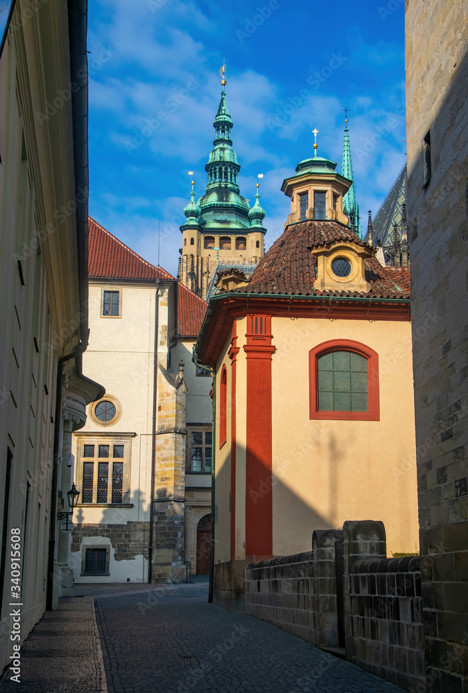 Fototapeta premium Empty narrow street in Prague castle. Chapel of John of Nepomuk and tower of St. Vitus Cathedral on background, Prague