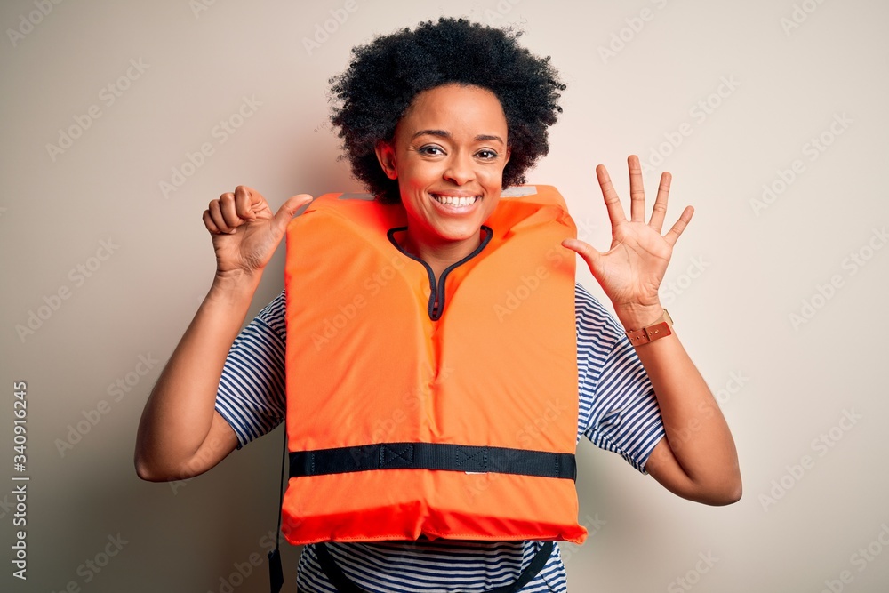 Young African American afro woman with curly hair wearing orange protection lifejacket showing and pointing up with fingers number six while smiling confident and happy. Young African American afro woman with curly hair wearing orange protection lifejacket showing and pointing up with fingers number six while smiling confident and happy.