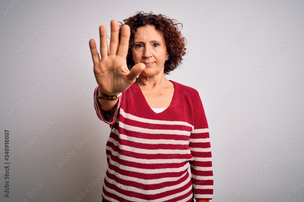 Middle age beautiful curly hair woman wearing casual striped sweater over white background doing stop sing with palm of the hand. Warning expression with negative and serious gesture on the face. Middle age beautiful curly hair woman wearing casual striped sweater over white background doing stop sing with palm of the hand. Warning expression with negative and serious gesture on the face.