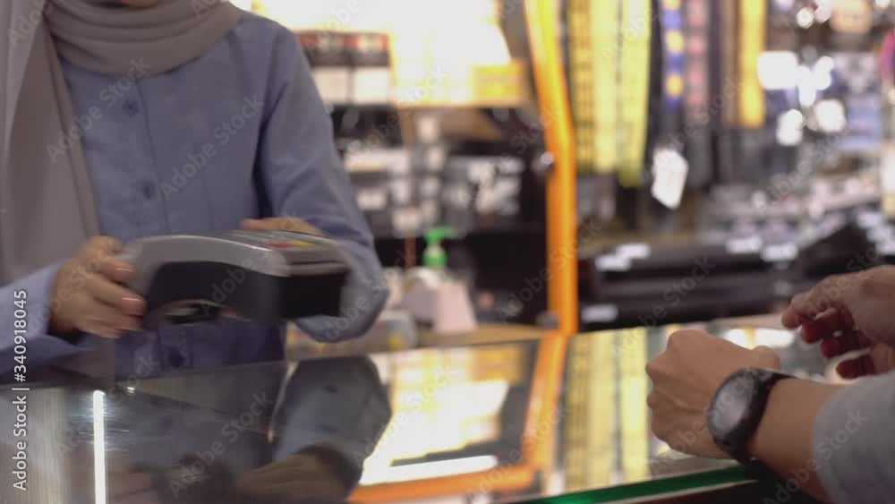 An upwardly mobile Asian Muslim man using a Smartwatch to pay for a product at a sale terminal with nfc identification payment for verification and authentication An upwardly mobile Asian Muslim man using a Smartwatch to pay for a product at a sale terminal with nfc identification payment for verification and authentication