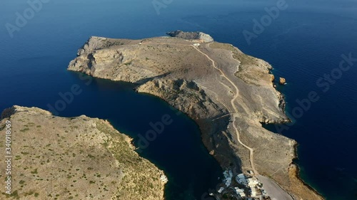 Aerial shot of a rocky cape on the Greek island of Sifnos. Camera flies back to reveal a small fishing village engulfed by two capes. photo