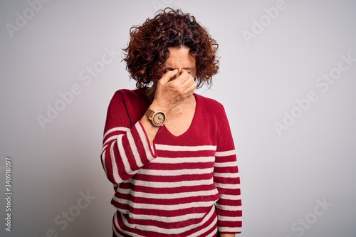 Middle age beautiful curly hair woman wearing casual striped sweater over white background tired rubbing nose and eyes feeling fatigue and headache. Stress and frustration concept. © Krakenimages.com