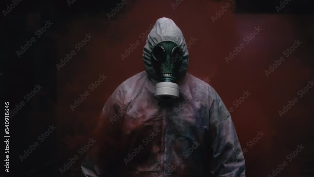 Adult In White Hazmat Suit Wearing Face Respirator Walking Through Red Smoke. Slow Motion, Follow Shot Adult In White Hazmat Suit Wearing Face Respirator Walking Through Red Smoke. Slow Motion, Follow Shot