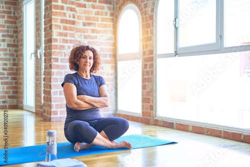 Middle age beautiful sportswoman wearing sportswear sitting on mat practicing yoga at home skeptic and nervous, disapproving expression on face with crossed arms. Negative person.