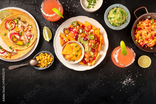 Mexican food, a flat lay on a dark background with a place for text. Nachos, tortillas, Paloma cocktails, guacamole and other dishes, overhead shot