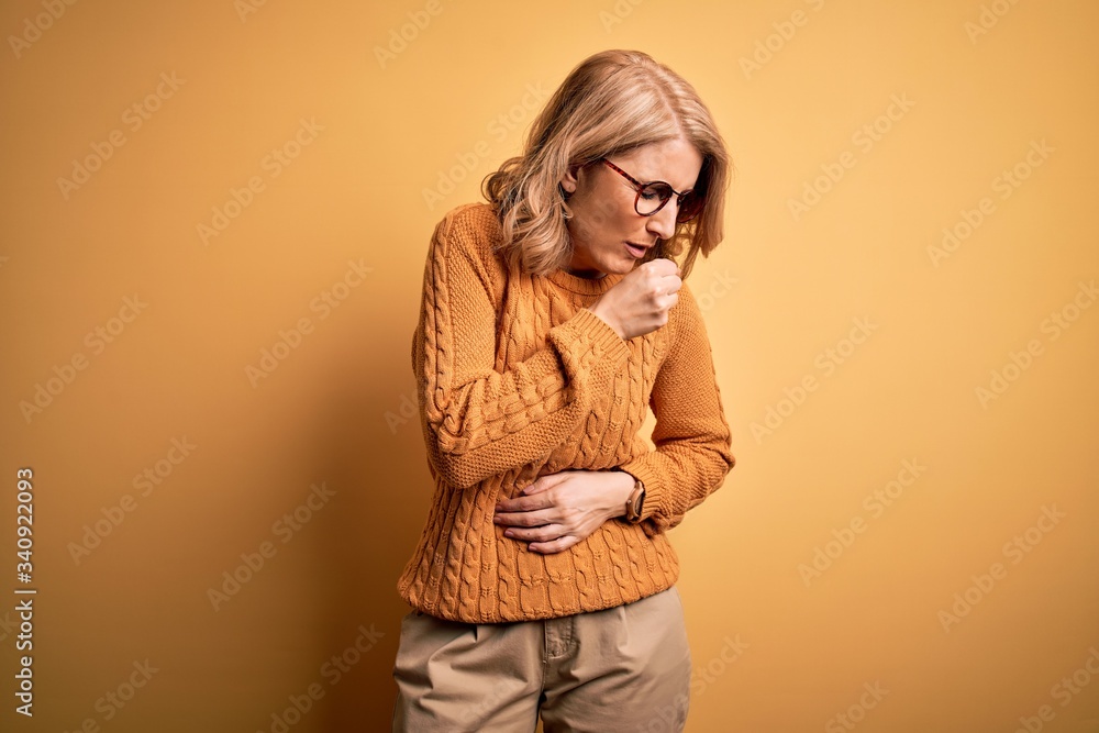 Middle age beautiful blonde woman wearing casual sweater and glasses over yellow background feeling unwell and coughing as symptom for cold or bronchitis. Health care concept. Middle age beautiful blonde woman wearing casual sweater and glasses over yellow background feeling unwell and coughing as symptom for cold or bronchitis. Health care concept.