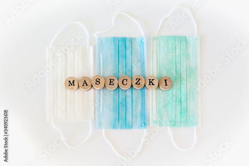 Words written with wooden blocks with black letters laying on protective surgical masks "Maseczki" means "masks" in polish.