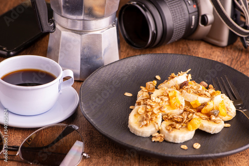 plate with sliced banana, granola, candied fruit and honey, toast and a cup of coffee