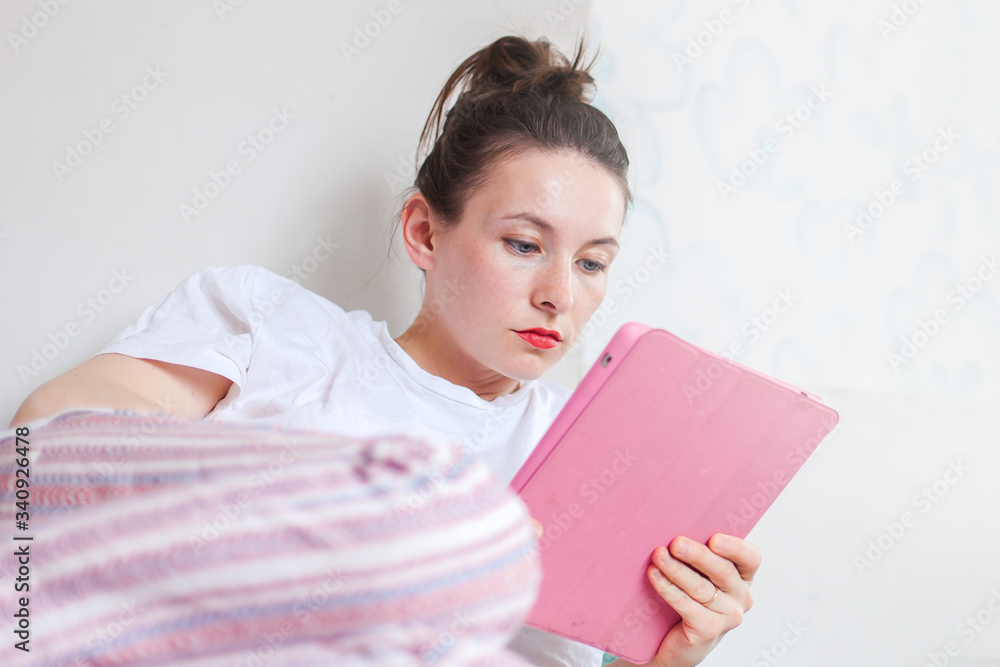 Young woman greets her friend online while lying in bed with a laptop, working from home, shopping online concept. Young woman greets her friend online while lying in bed with a laptop, working from home, shopping online concept.