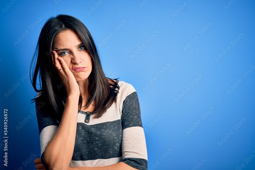 Young brunette woman with blue eyes wearing casual striped t-shirt standing over background thinking looking tired and bored with depression problems with crossed arms. Young brunette woman with blue eyes wearing casual striped t-shirt standing over background thinking looking tired and bored with depression problems with crossed arms.