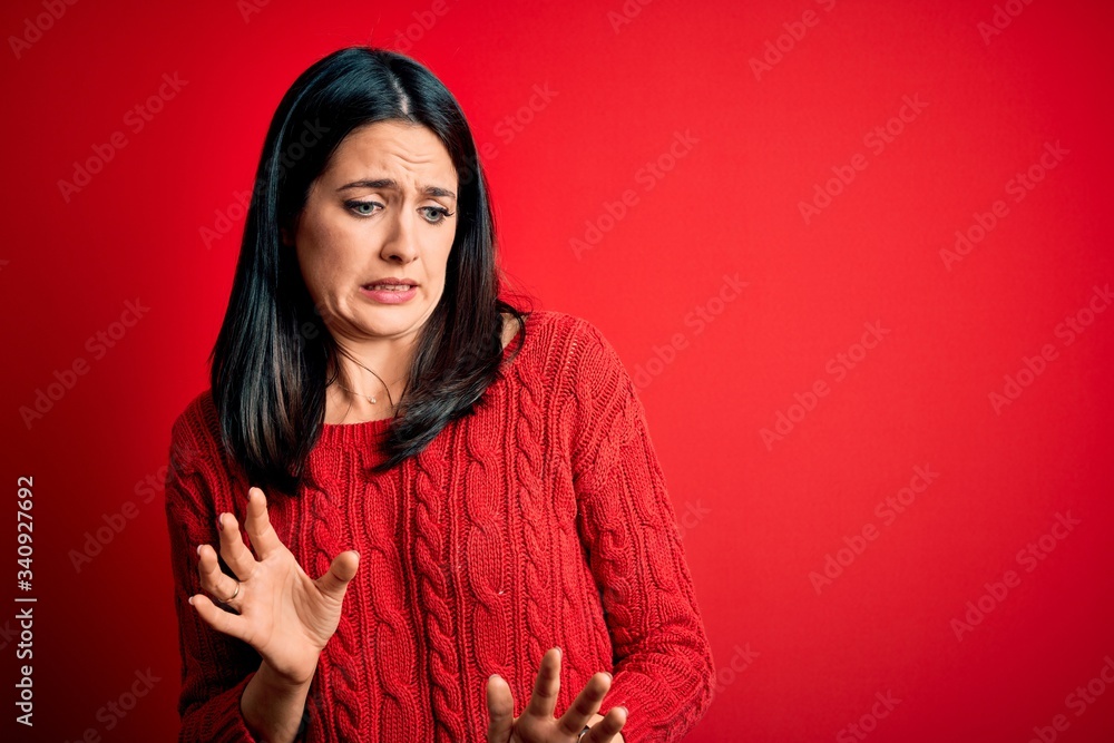 Young brunette woman with blue eyes wearing casual sweater over isolated red background disgusted expression, displeased and fearful doing disgust face because aversion reaction. Young brunette woman with blue eyes wearing casual sweater over isolated red background disgusted expression, displeased and fearful doing disgust face because aversion reaction.
