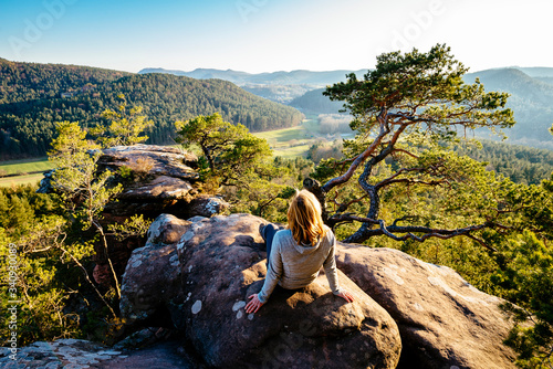 A blonde woman sits on a sandstone cliff in the Palatinate Forest and looks at the sunset photo