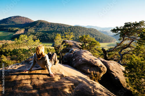 Canvas Print A blonde woman sits on a sandstone cliff in the Palatinate Forest and looks at t