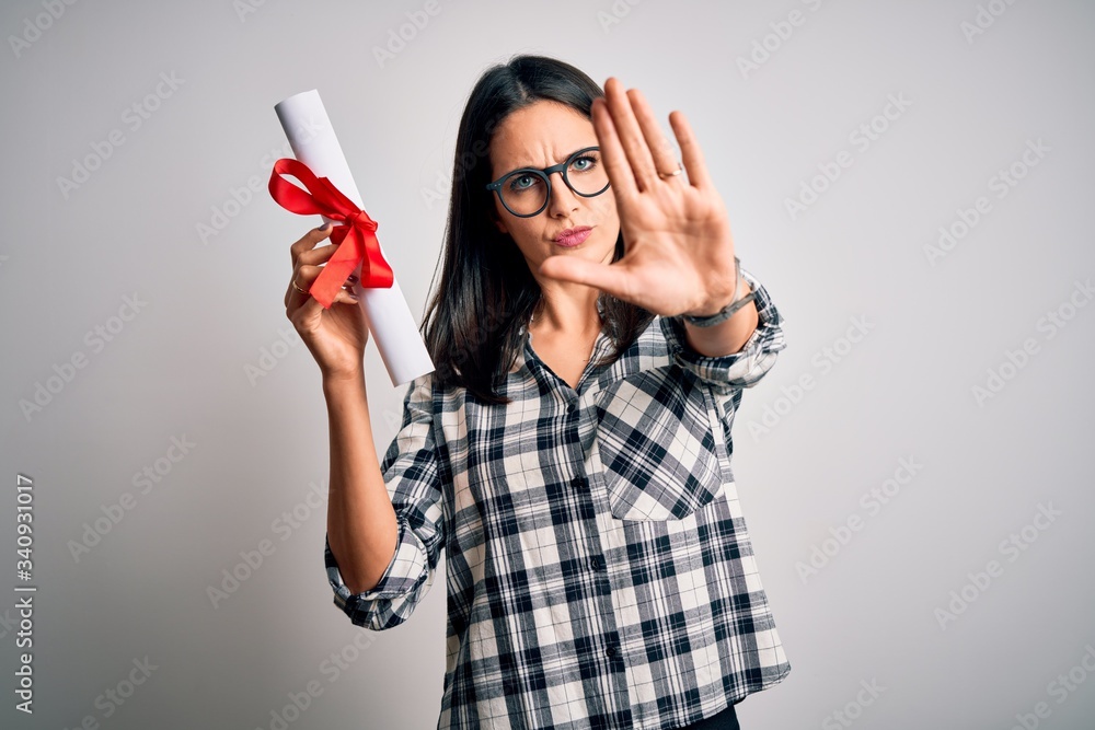 Young brunette student woman with blue eyes holding university diploma over isolated background with open hand doing stop sign with serious and confident expression, defense gesture Young brunette student woman with blue eyes holding university diploma over isolated background with open hand doing stop sign with serious and confident expression, defense gesture