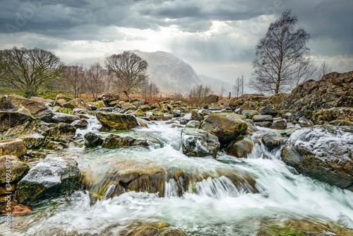Stormy clouds and rain with a fluttering of fallen snow over Langstrath Beck in winter on the Cumbria Way footpath near Rosthwaite in Borrowdale  Lake District National Park  Cumbrian Mountains  Cumbr