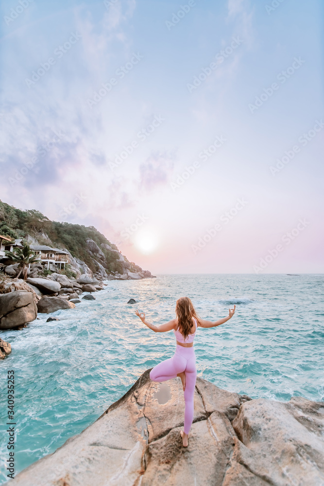 Pregnant woman practices yoga, standing in vrksasana position on the beach, on the rocks. Hands of girl in a pose meditating. Serenity practicing at sunrise, meditation. Woman in pink-purple tracksuit Pregnant woman practices yoga, standing in vrksasana position on the beach, on the rocks. Hands of girl in a pose meditating. Serenity practicing at sunrise, meditation. Woman in pink-purple tracksuit