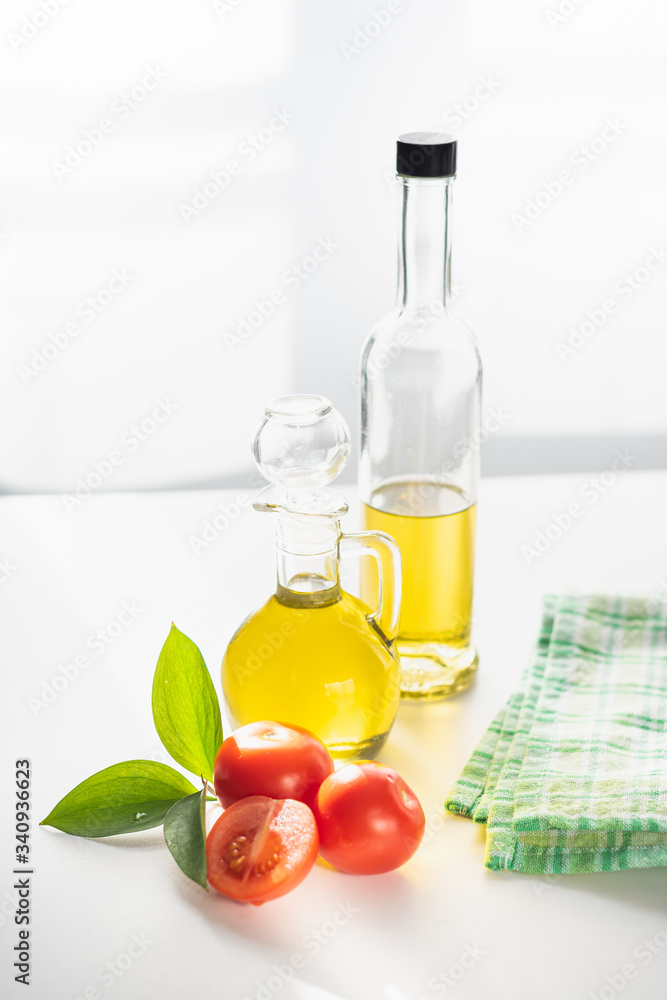 on a white background vegetable olive oil in a glass decanter. Nearby are slices of tomatoes and a green leaf. on a white background vegetable olive oil in a glass decanter. Nearby are slices of tomatoes and a green leaf.