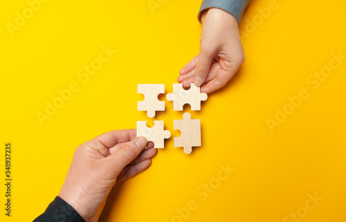 Two hands connect puzzles on a yellow background. Cooperation and teamwork in business. Collaboration people for success.