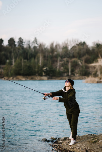 Woman catching a fish on lake or pond with text space. Fisherman with rod throws bait into the water on river bank. Fishing for pike, perch, carp. Background wild nature. The concept of rural getaway.