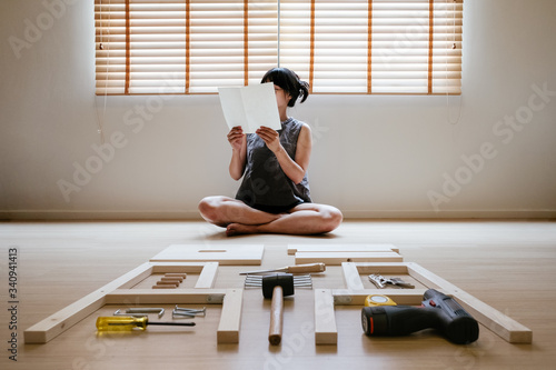 Young asian woman self assembly wooden furniture and read blank white paper to put instruction photo