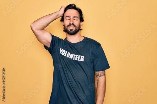 Young handsome hispanic volunteer man wearing volunteering t-shirt as social care smiling confident touching hair with hand up gesture, posing attractive and fashionable