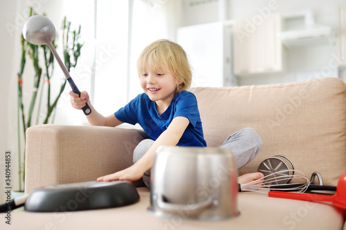 Mischievous preschooler boy play the music using kitchen tools and utensils at home during quarantine. Funny drum part from child. Entertainment a kids at home. photo