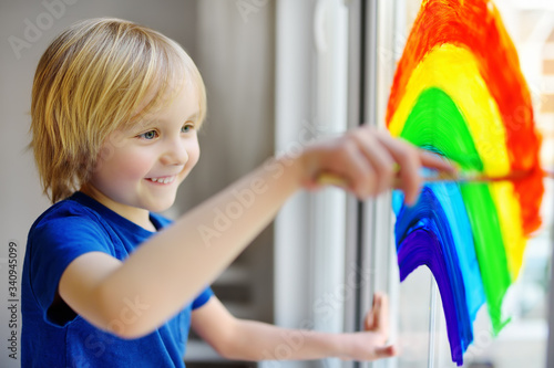 Little boy drawing on window rainbow while coronavirus quarantine. Rainbow sign is symbol of hope, means that everything will be OK. photo