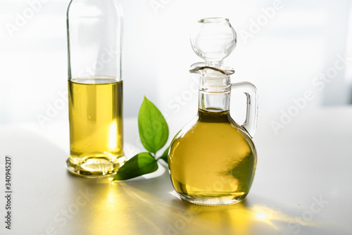 against the window, olive oil in a decanter and in a glass bottle, with a green leaf