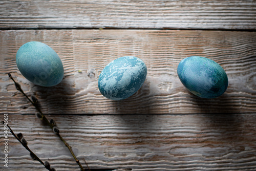 colored marble eggs lie in a cup, next to a willow branch, as a symbol of Easter, on a wooden table. rustic 