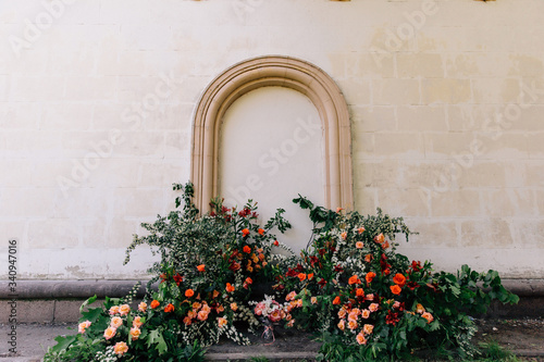 Fototapeta Naklejka Na Ścianę i Meble -  the unusual area of the wedding venue on the background of the wall with stucco is decorated with fresh flowers in the form of thickets and the main color accent coral