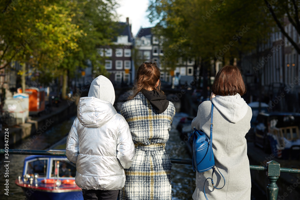 Tourists standing on a bridge looking at an Amsterdam canal