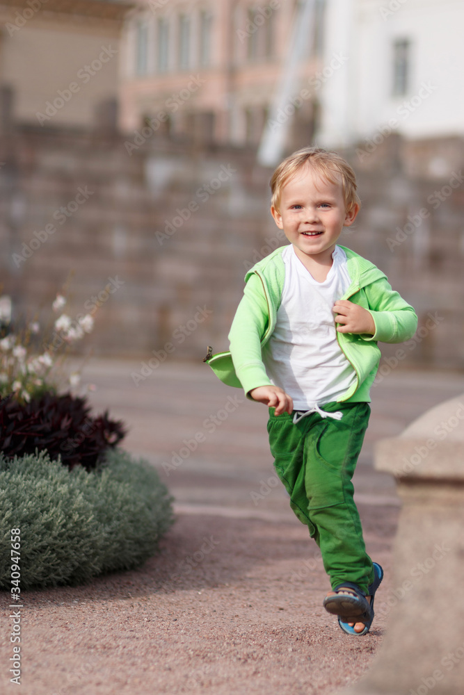 Fototapeta premium A blond child of European appearance in green clothes happy runs along the Senate Square in Helsinki in Finland.