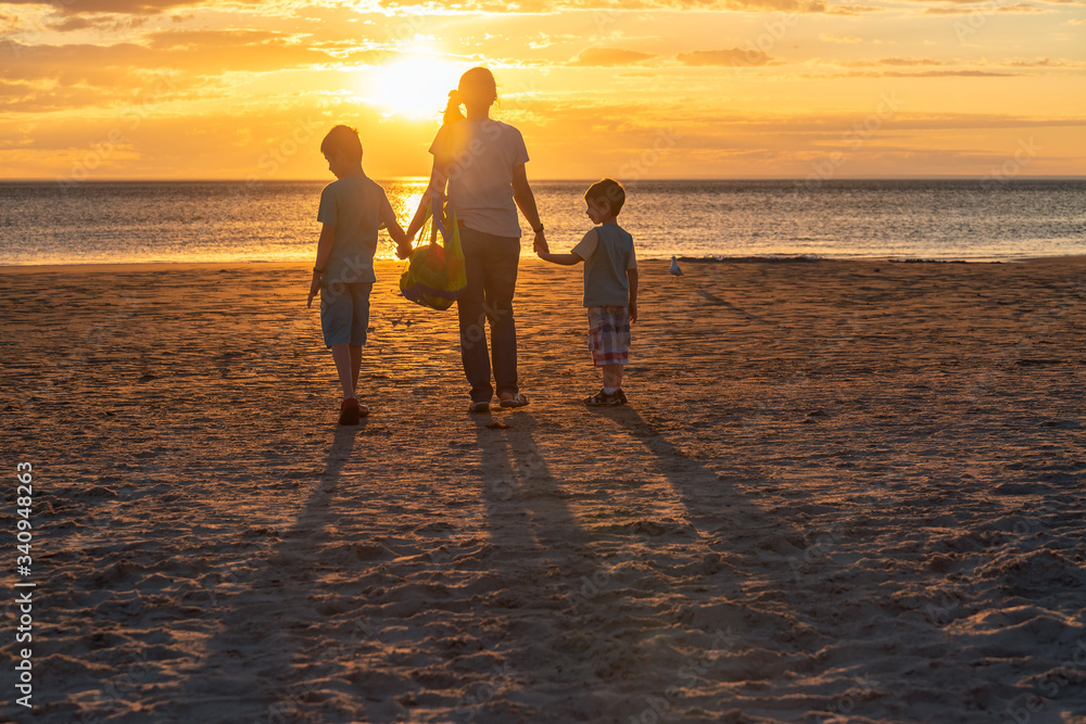 Mother with kids walking to the beach at sunset while carrying a bag full of toys, South Australia