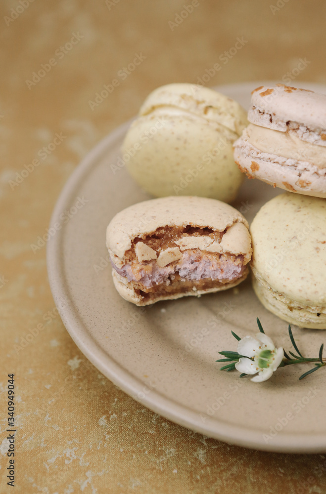 Yellow homemade macarons with blossom are lying on the brown plate on the golden background. Yellow homemade macarons with blossom are lying on the brown plate on the golden background.