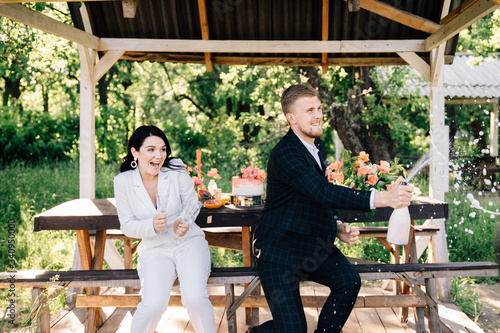 bride and groom sitting at a table outdoors open champagne with splashes and joy © nastya_shemet