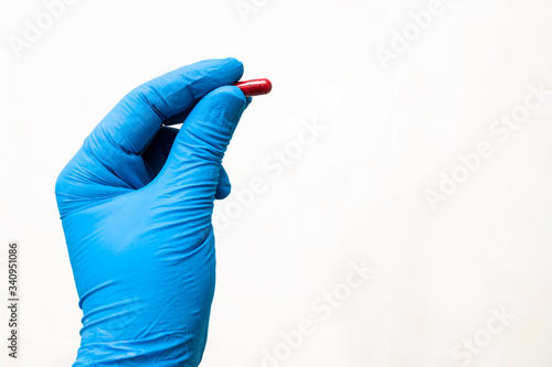 Hand of doctor with blue protecting glove giving a red pill. Healing concept.