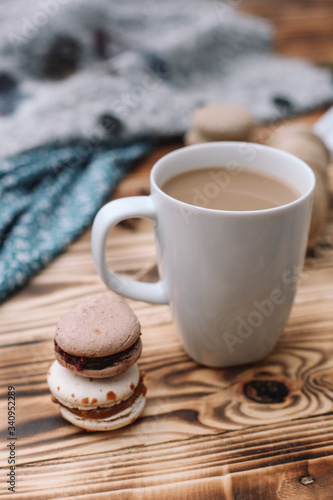 Two homemade colorful macaroons are lying on the brown wooden table with cup of coffee. Cup of coffee. Colorful tissue.