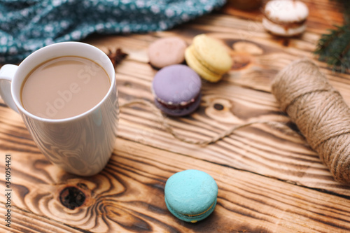 Homemade colorful macaroons are lying on the brown wooden table with cup of coffee. Cup of coffee. Anise, honey and colorful tissue.