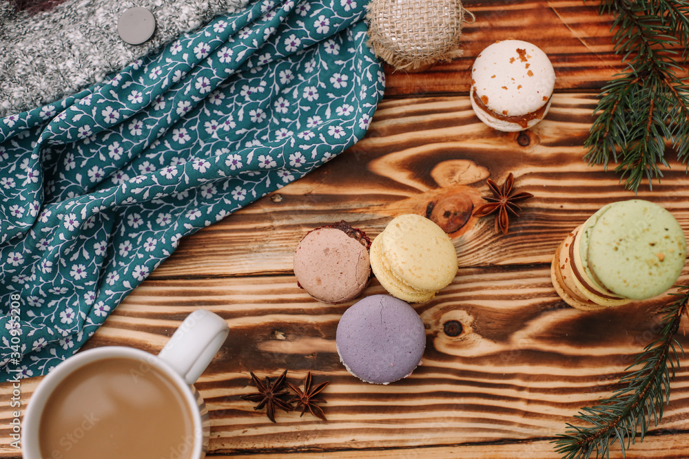 Homemade colorful macaroons are lying on the brown wooden table with cup of coffee. Cup of coffee. Anise, honey and colorful tissue.