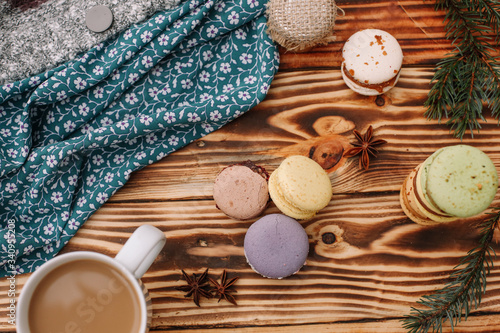 Homemade colorful macaroons are lying on the brown wooden table with cup of coffee. Cup of coffee. Anise  honey and colorful tissue.