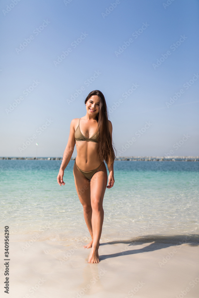 Young girl in white bikini walking at tropical beach