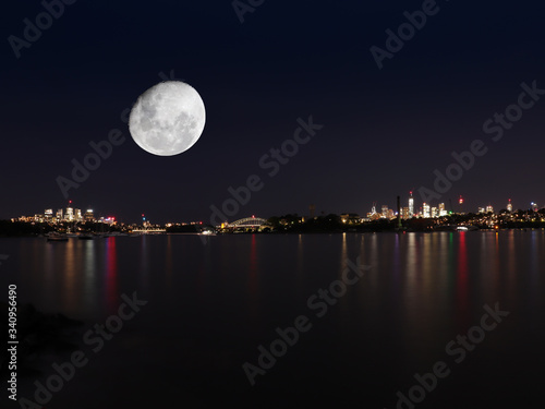 Sydney harbour illuminated by the moon and circular quay with vibrant colourful lights at midnight in NSW Australia