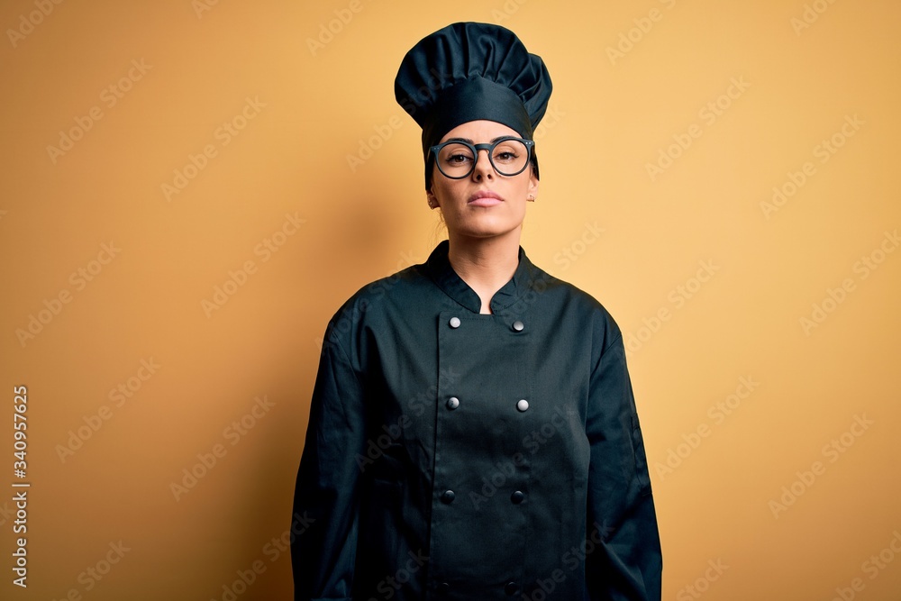 Young beautiful brunette chef woman wearing cooker uniform and hat over yellow background Relaxed with serious expression on face. Simple and natural looking at the camera. Young beautiful brunette chef woman wearing cooker uniform and hat over yellow background Relaxed with serious expression on face. Simple and natural looking at the camera.