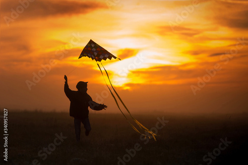 Flying a kite. The boy runs across the field with a kite. Silhouette of a child against the sky. Bright sunset.