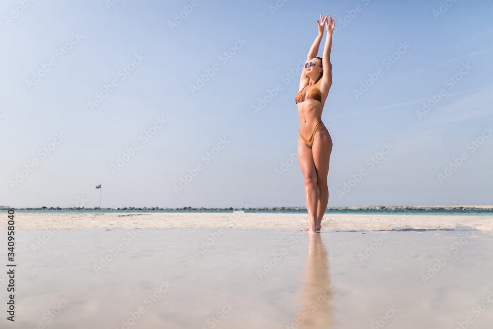 Full length portrait of beautiful happy girl standing in sea. Young happy cheerful woman in bikini smiling, enjoying sun, summer vacation, freedom, raising her hands up, looking at camera Full length portrait of beautiful happy girl standing in sea. Young happy cheerful woman in bikini smiling, enjoying sun, summer vacation, freedom, raising her hands up, looking at camera