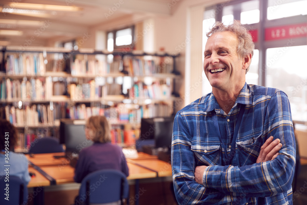 Obraz premium Portrait Of Mature Male Teacher Or Student In Library With Other Students Studying In Background